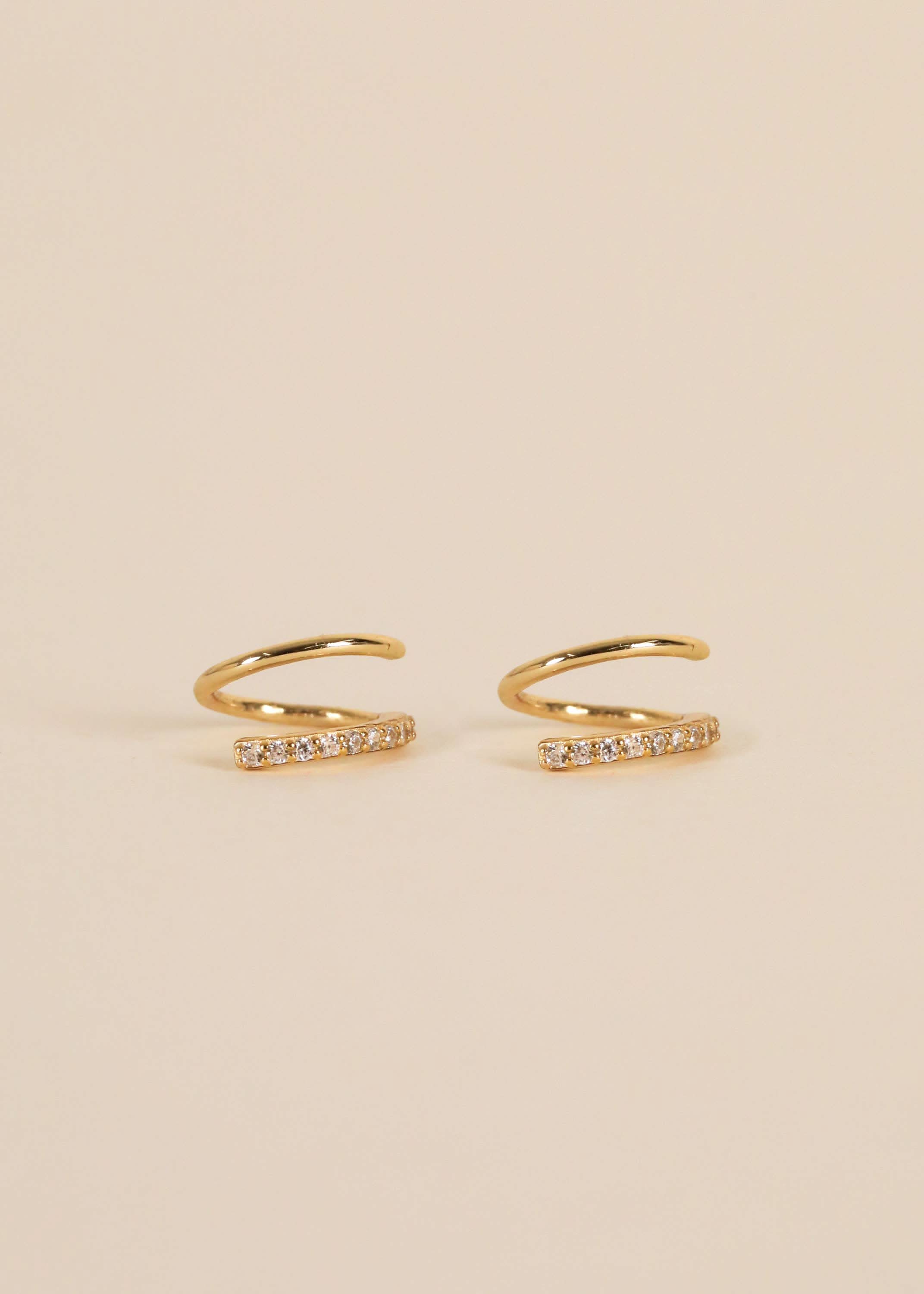 Gold pave spiral earrings from Jaxkelly sitting against cream background 
