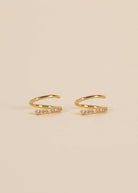 Gold pave spiral earrings from Jaxkelly sitting against cream background 