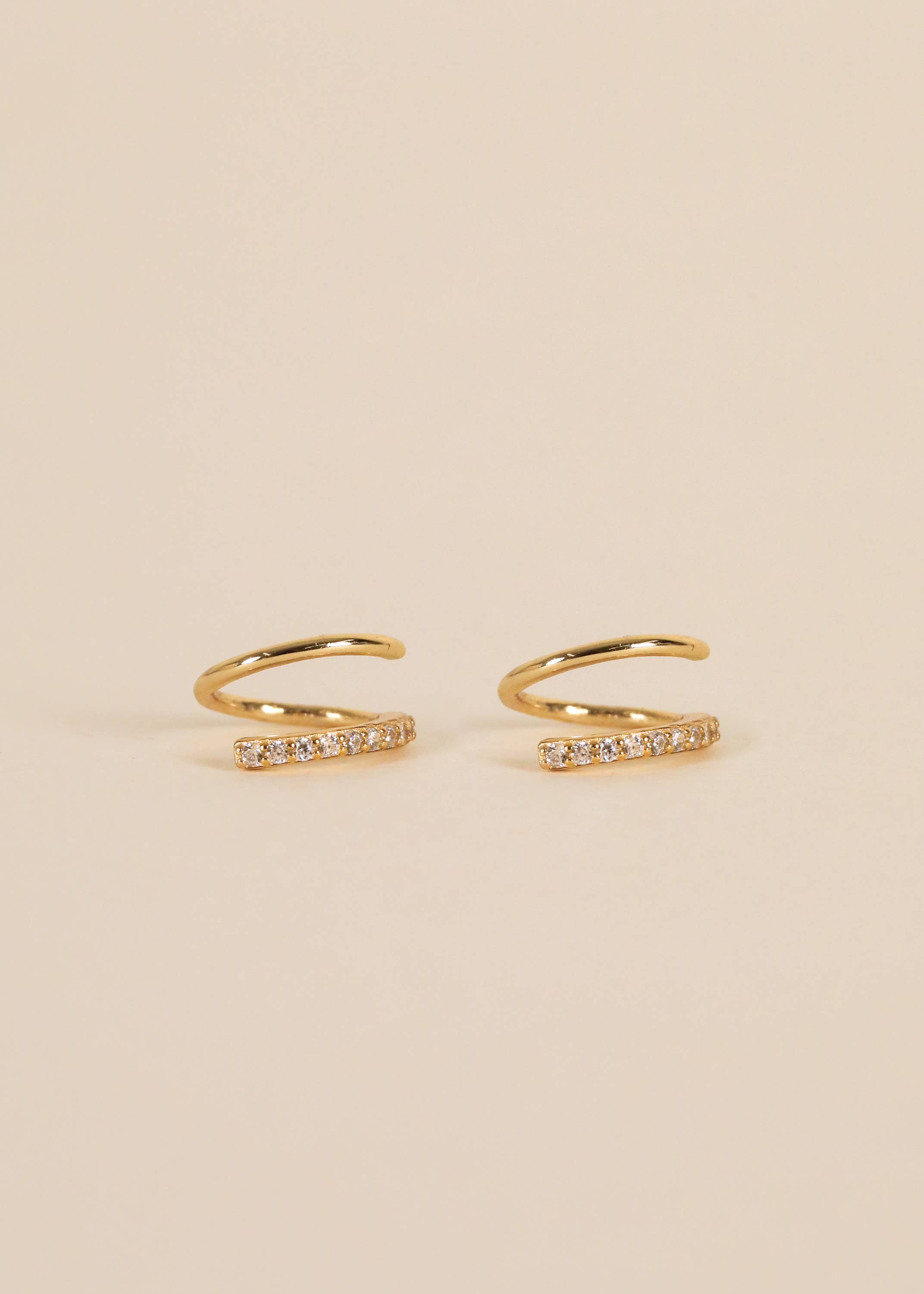 Gold pave spiral earrings from Jaxkelly sitting against cream background 