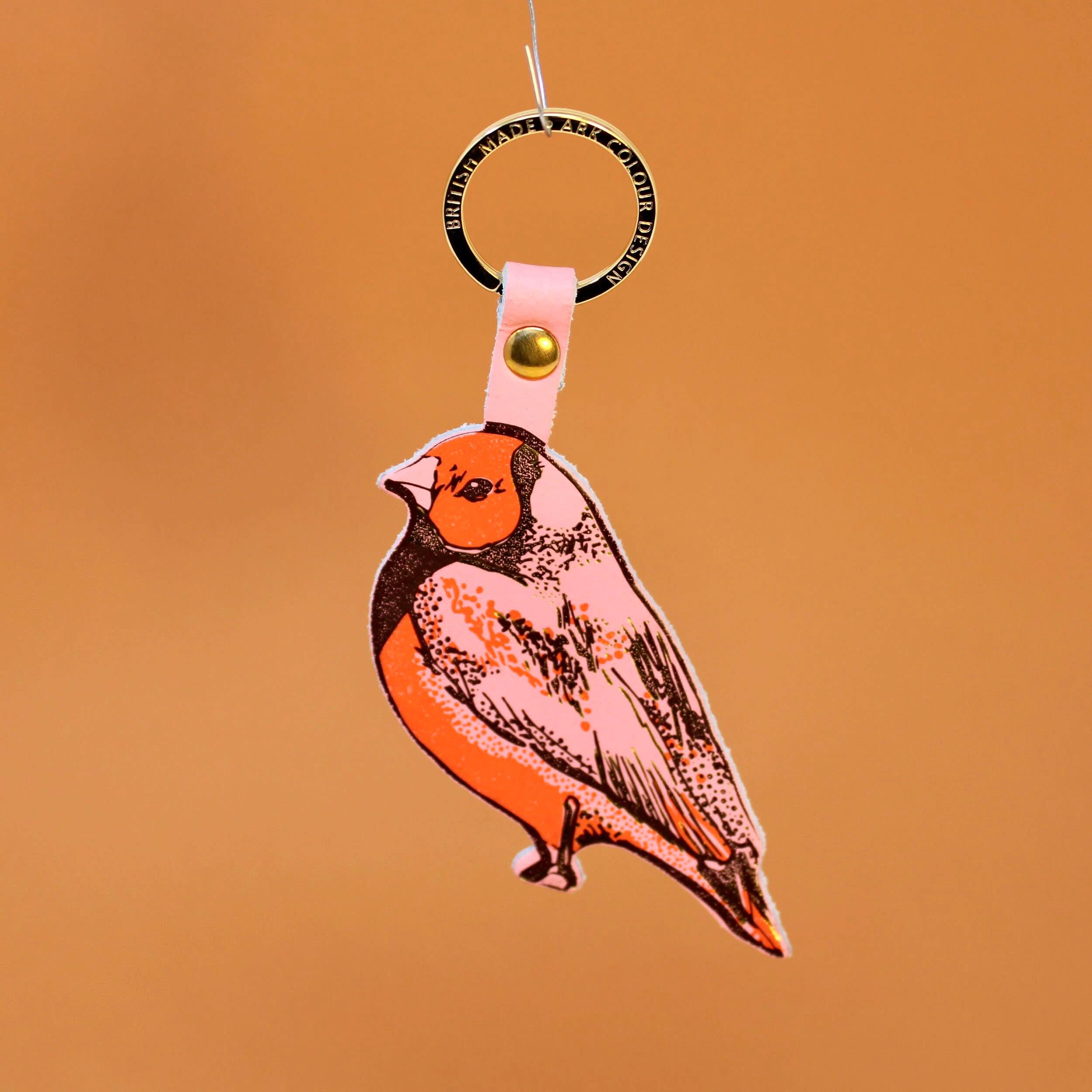 Colorful finch bird keychain behind an orange background. 
