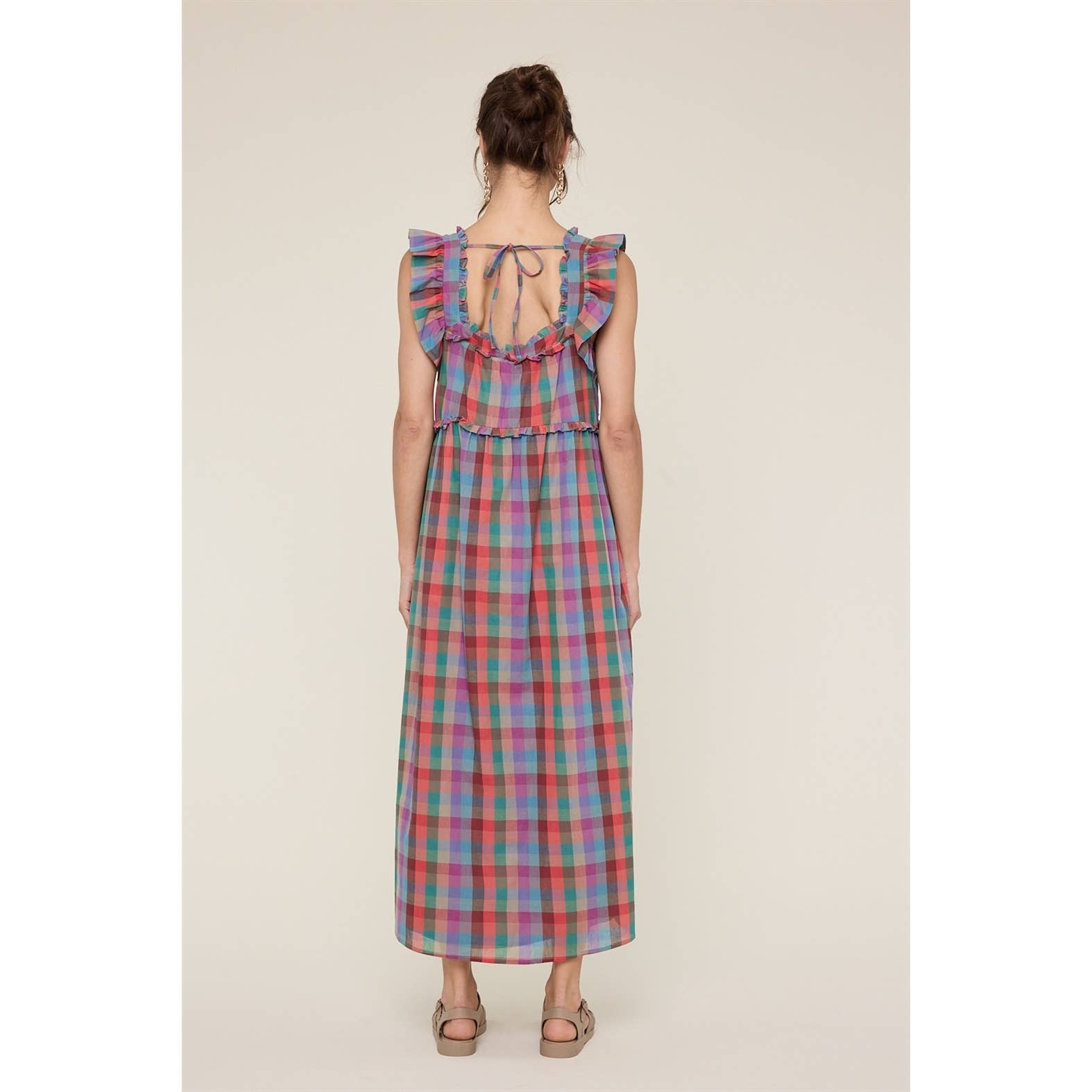 Woman wearing a colorful plaid dress with ruffled straps on a beige background