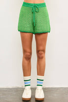 Woman wearing tube socks, tennis shoes, and green tie waist sweater shorts with dark green lining and light green and yellow details 