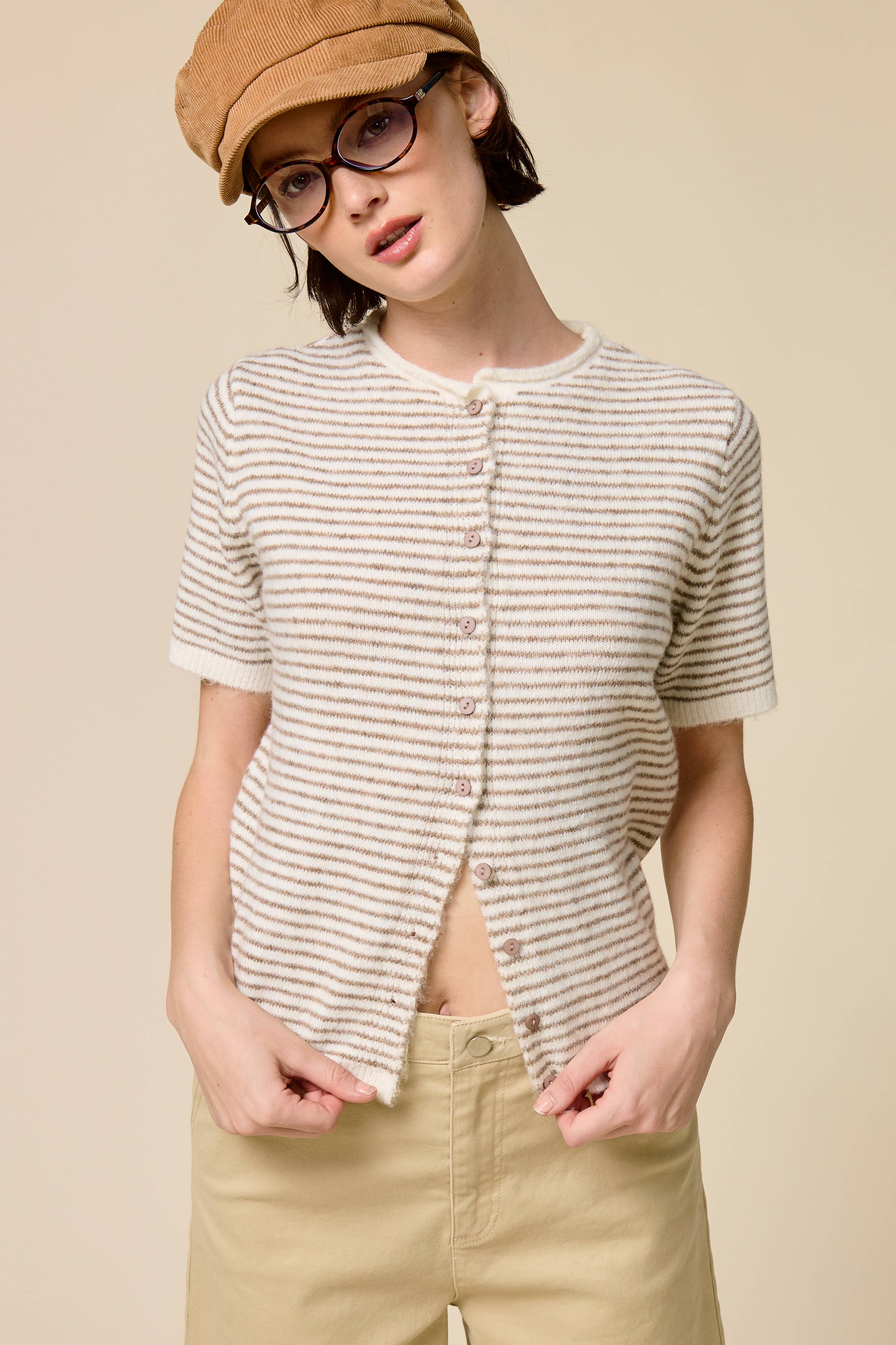 Person wearing a striped shirt, beige cap, and glasses on a beige background