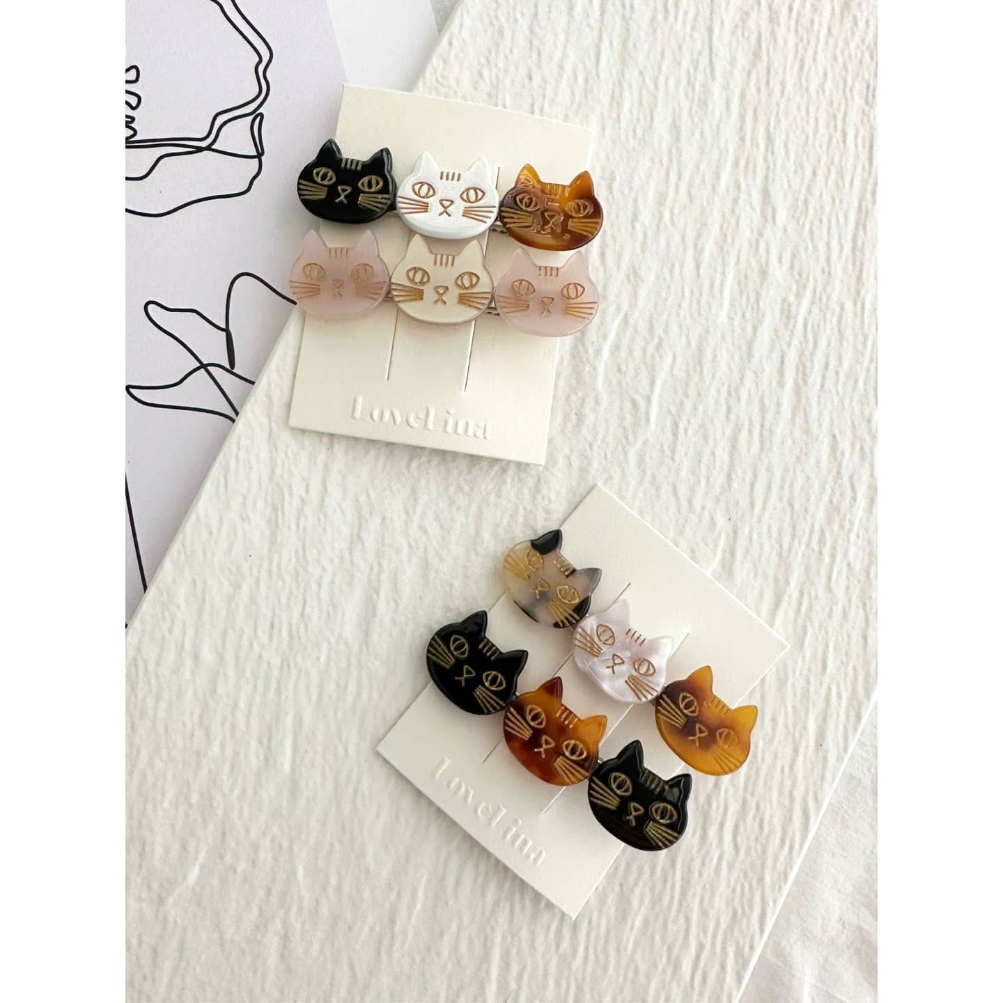 Two pairs of three colorful cats on a clip in a pack of two behind a white and purple background. 