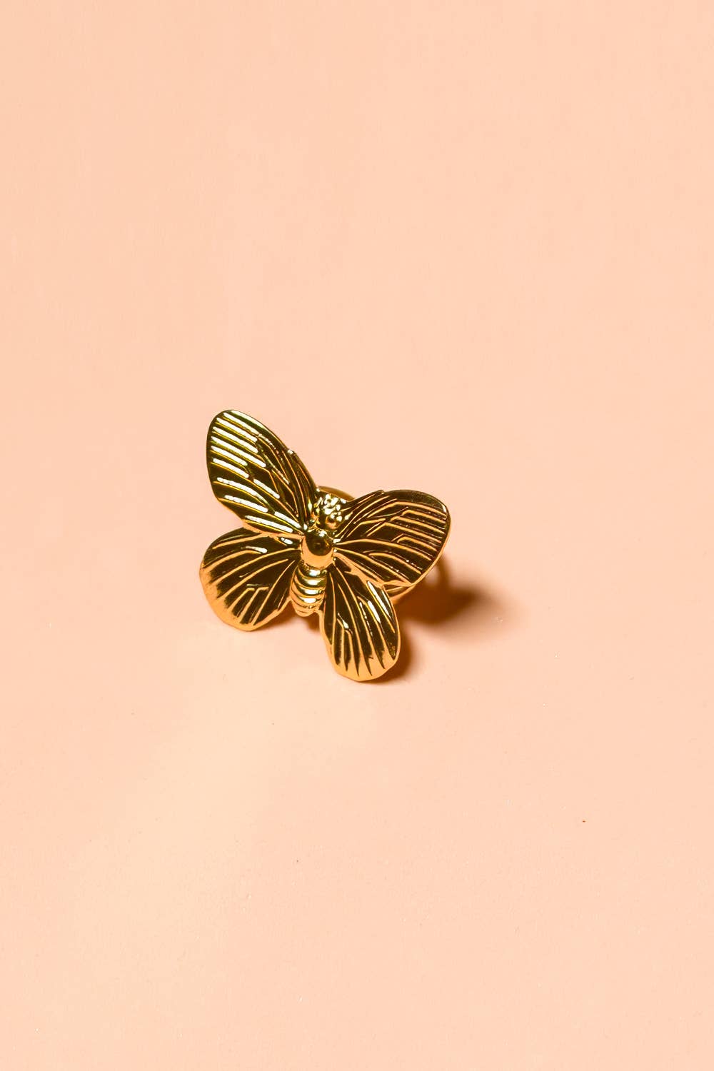 Chunky Gold butterfly ring with ridges on the wings set up on a pink background 