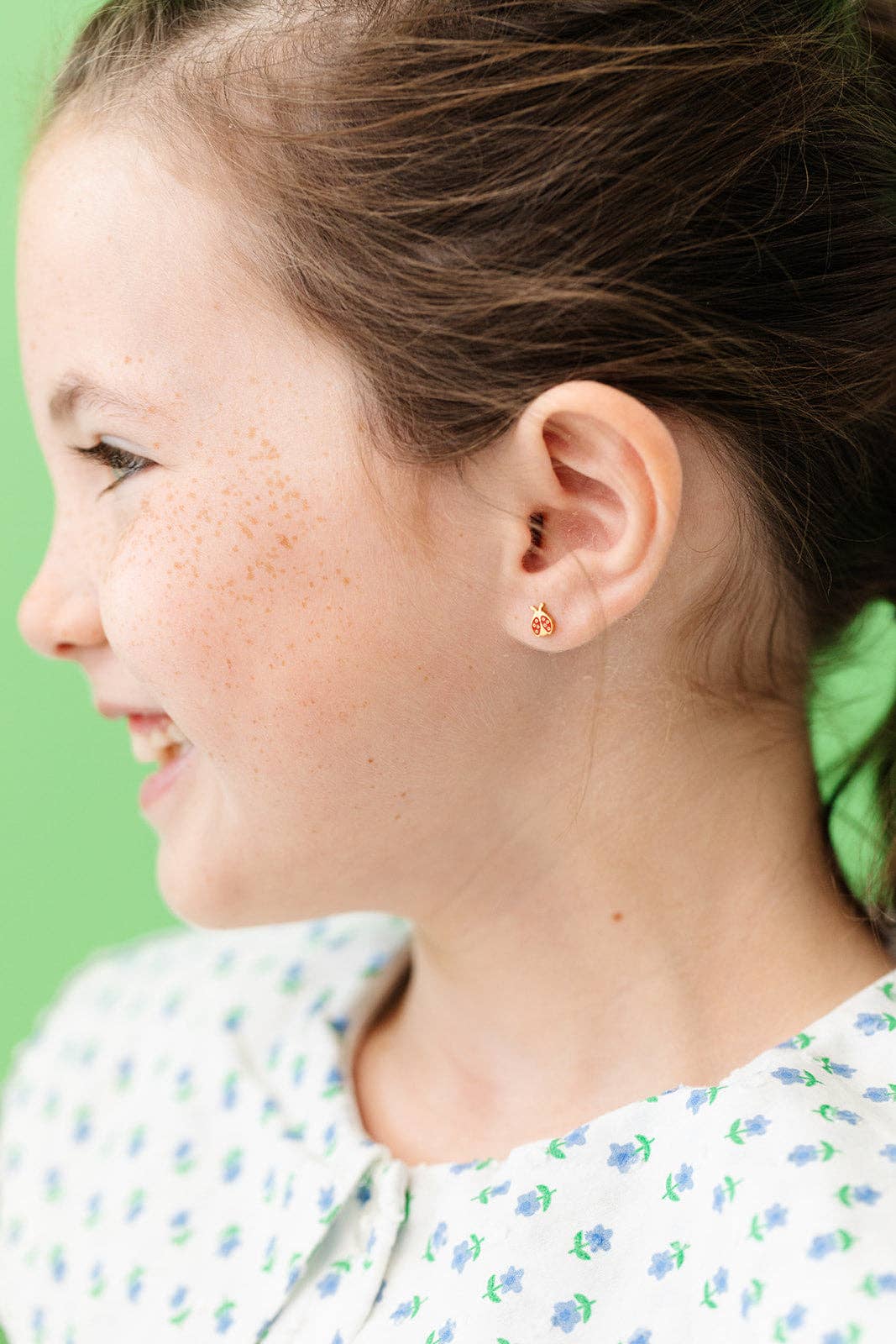 Child wearing a Pair of red and gold ladybug flat back earrings laying on a white surface 