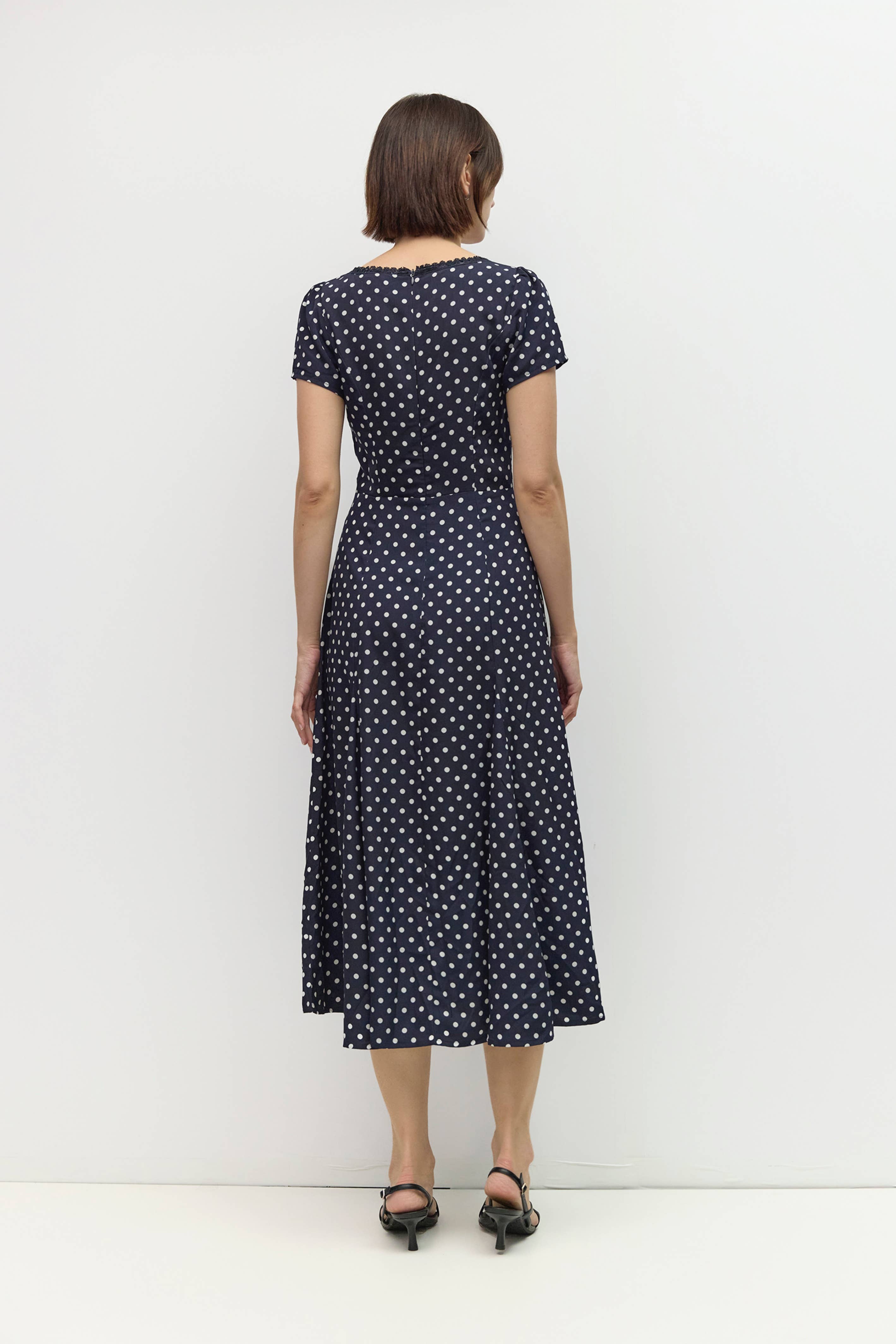 Woman wearing a navy dress with white polka dots against a white background