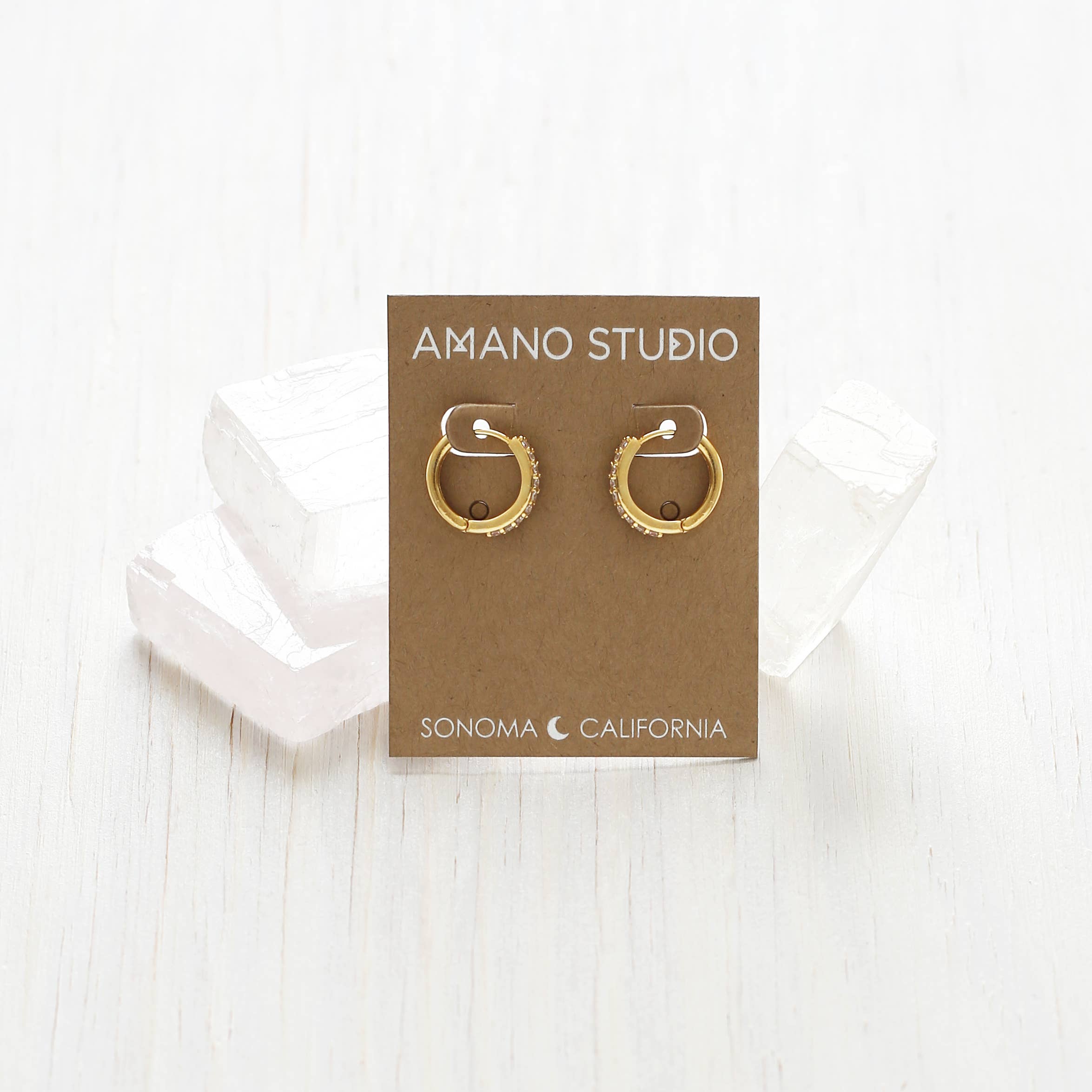 Gold hoop earrings on a brown AMANO STUDIO card with 'Sonoma, California' text on a white background