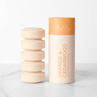 Stacked orange cedar wood shower steamer tablets next to packaging 