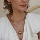 woman wearing white blouse and gold puffed heart necklace