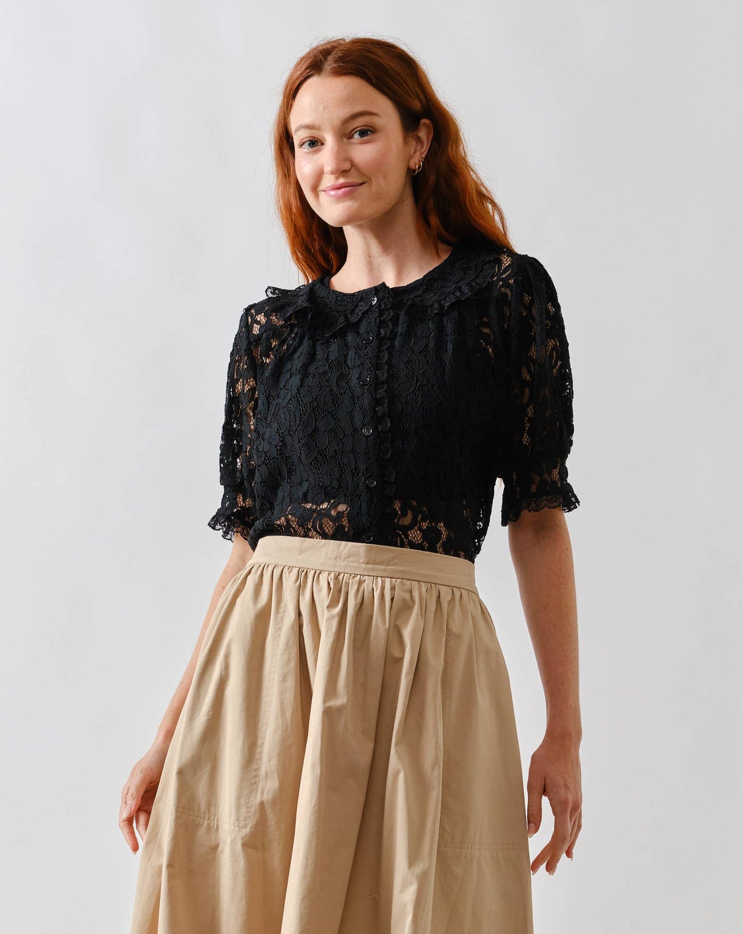 Woman wearing a black lace top and beige skirt on a white background