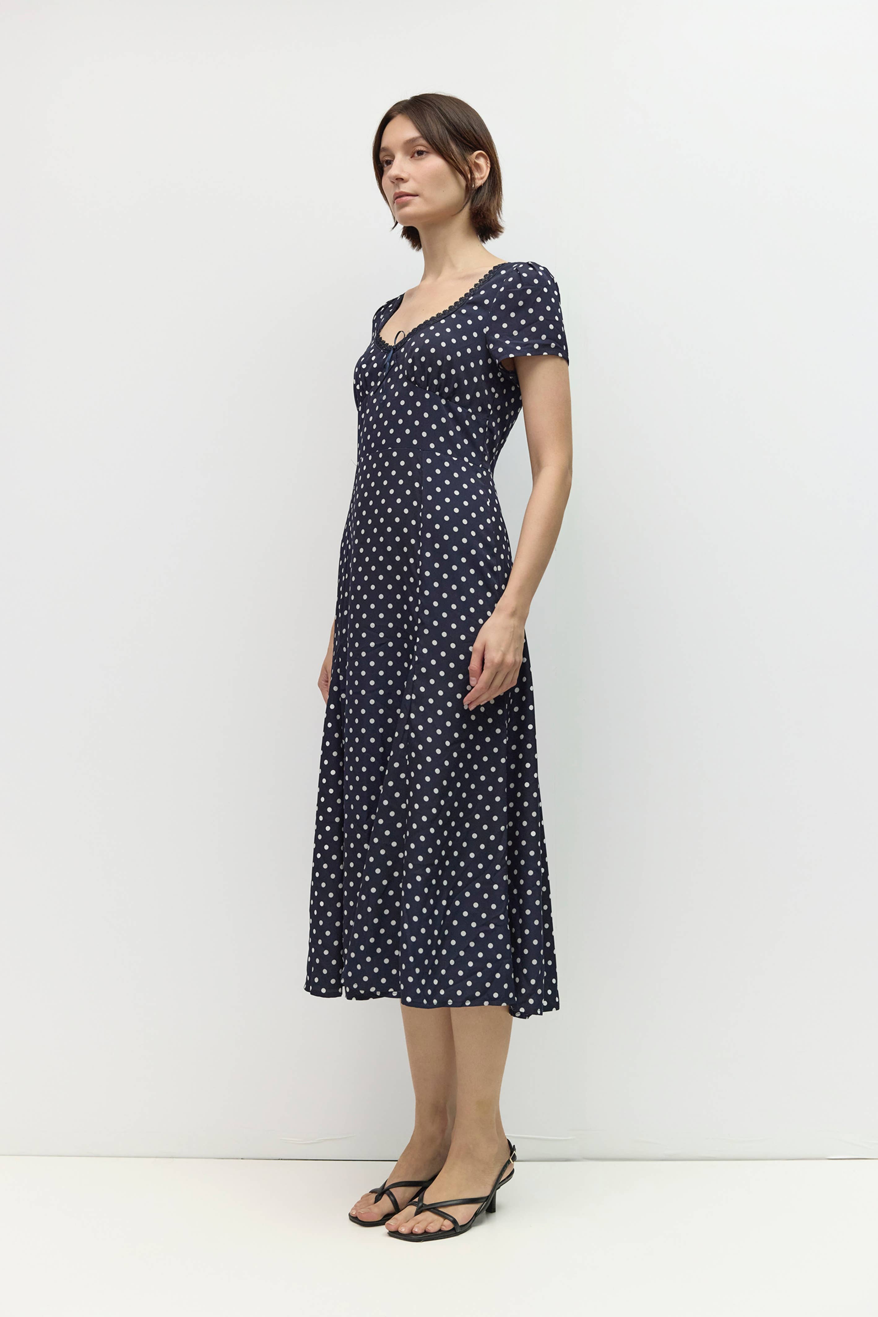 Woman wearing a navy dress with white polka dots against a white background