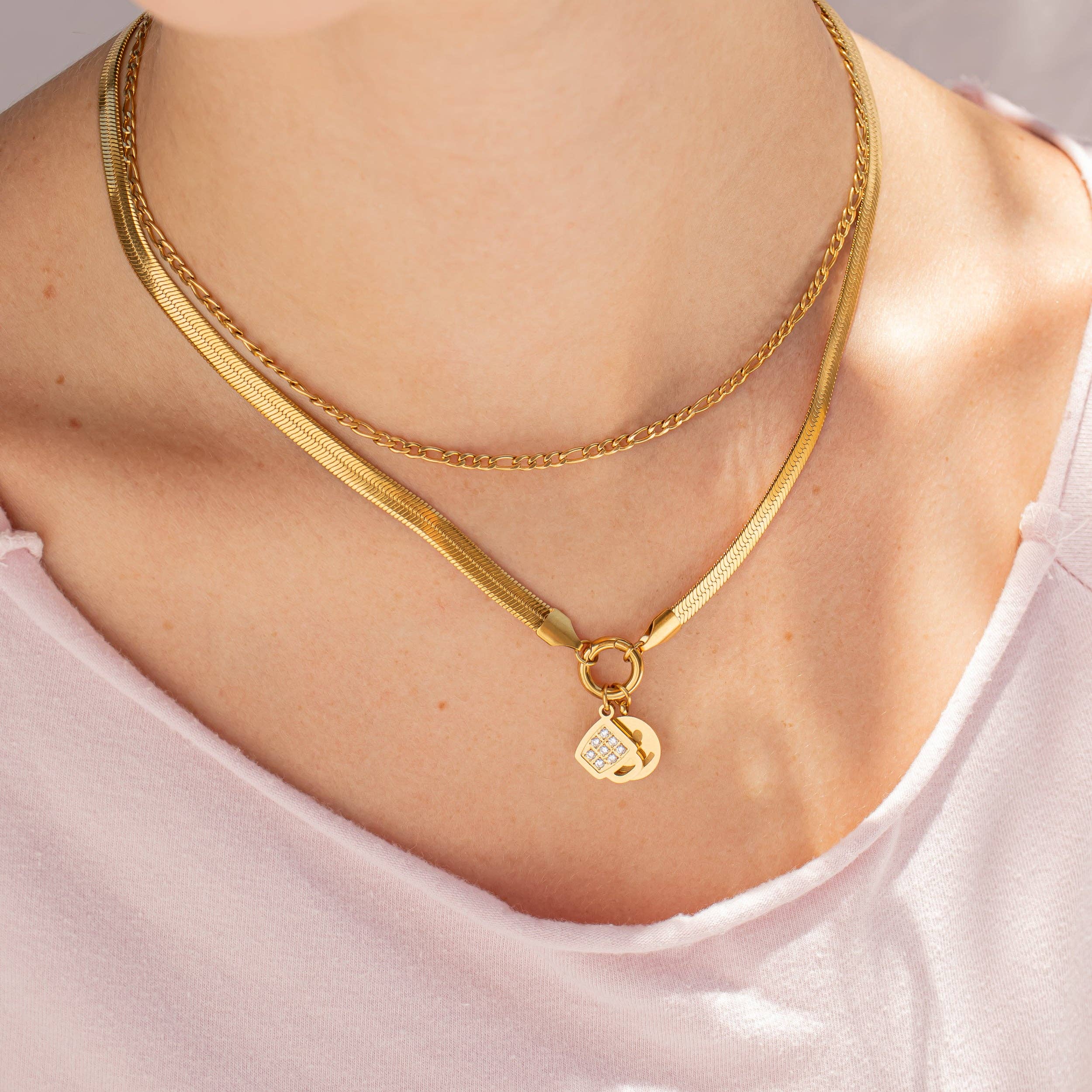 Gold necklace with a heart pendant on a person wearing a light pink top.