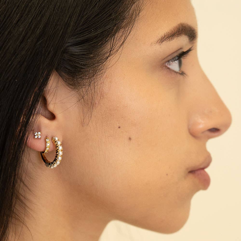 Close-up of a person wearing gold hoop earrings with a neutral background