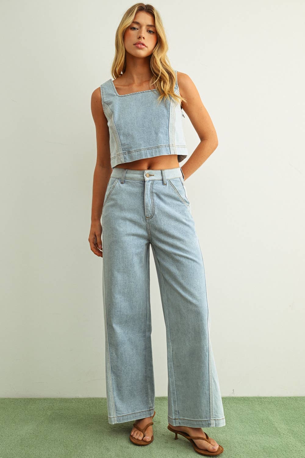 Woman wearing light denim jeans and light denim top standing behind a white background