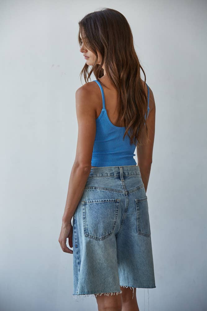 Woman wearing a blue tank top and denim skirt against a plain background