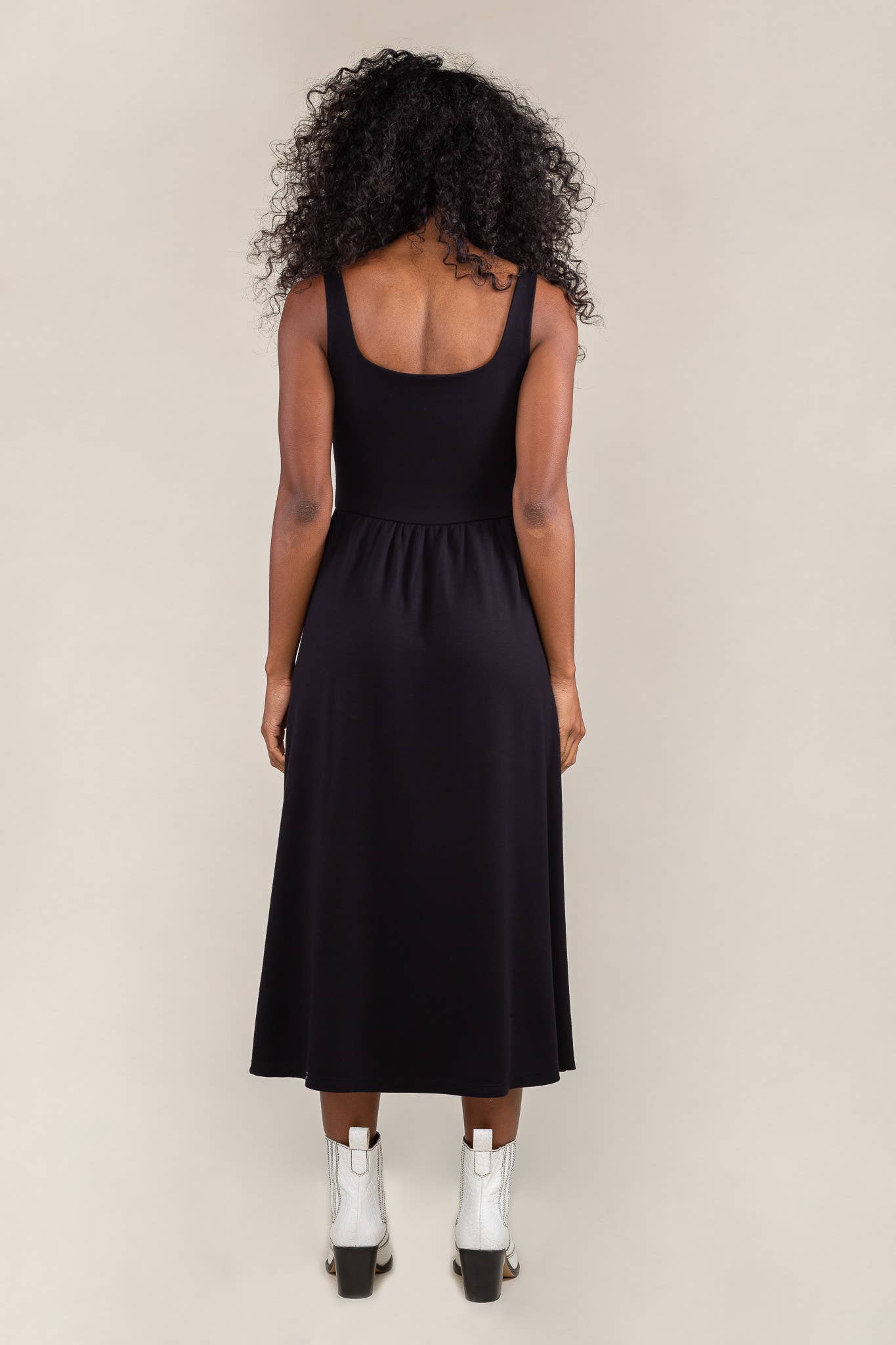 Woman facing away from the camera wearing black colored, midi dress, with corset bodice detail 
