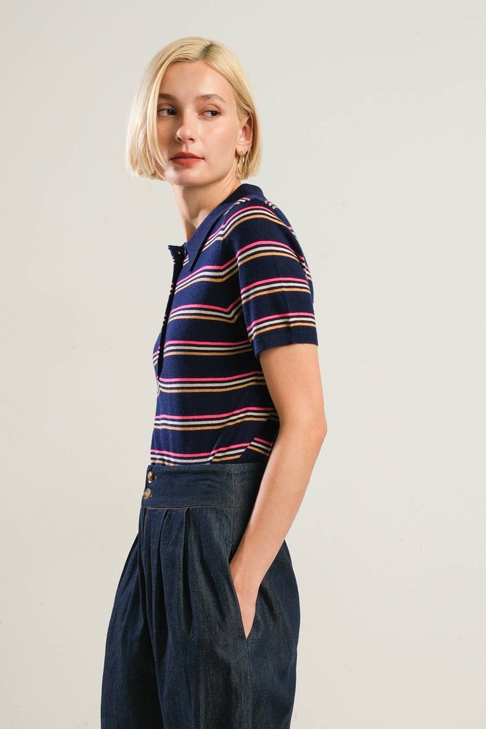 Woman wearing a striped polo shirt and navy pants against a plain background