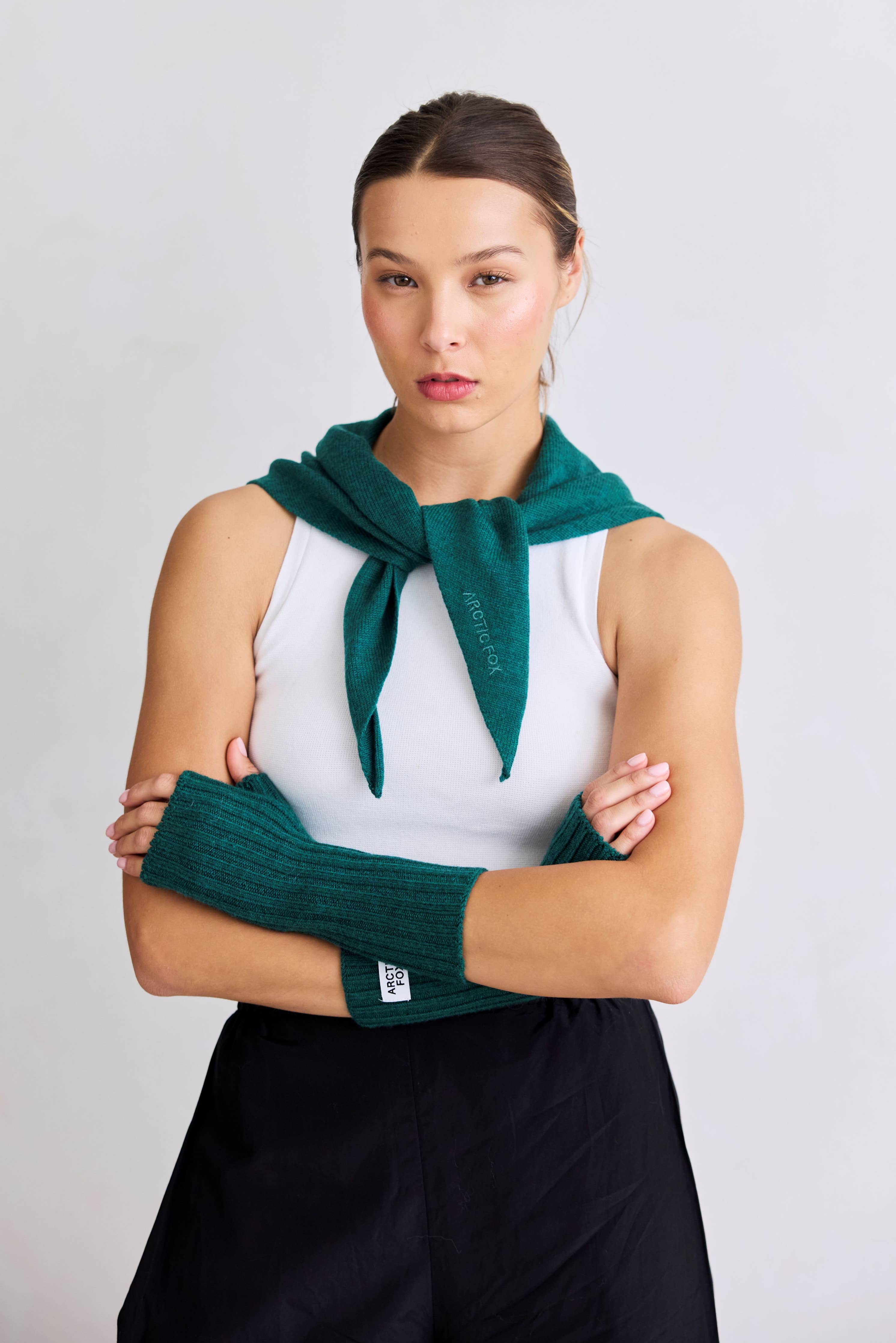 Woman wearing a green knitted scarf and arm warmers against a plain background
