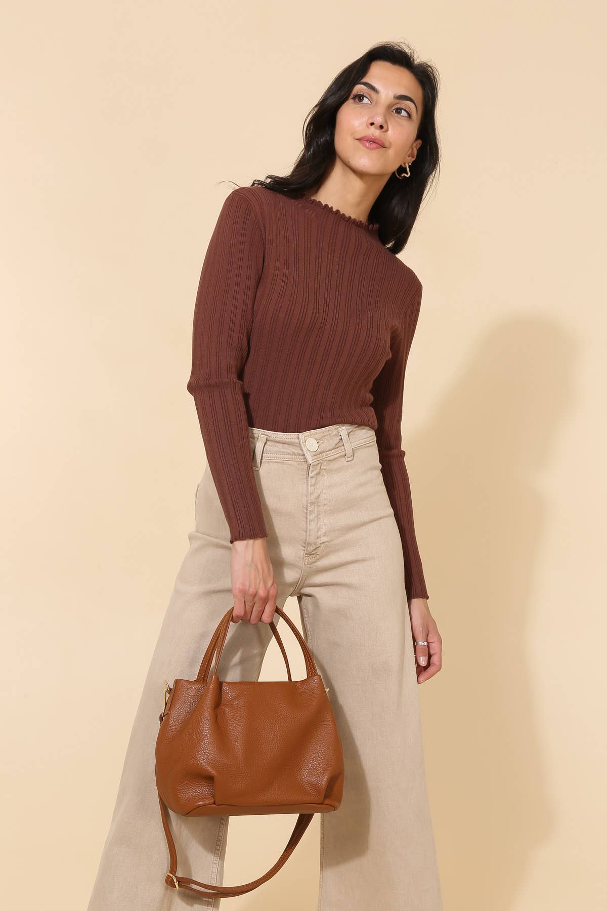 Model wearing plum red and beige carrying Big chestnut brown leather handbag purse with handles, strap, and gold details 