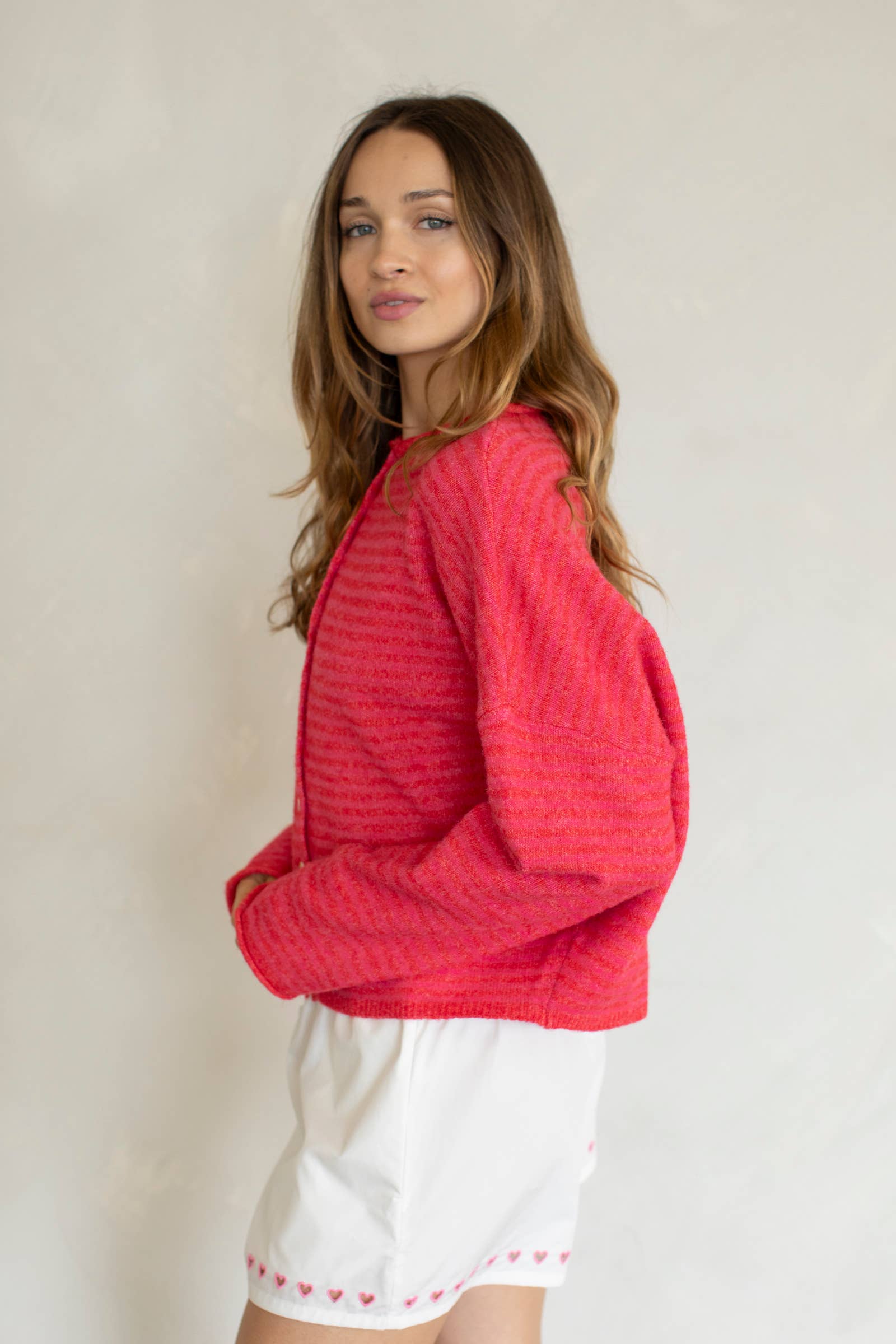 Woman wearing a red textured sweater and white shorts with a light background