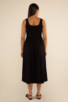 Woman facing away from the camera wearing black thick tank strapped top dress with full bodice and low drop skirt