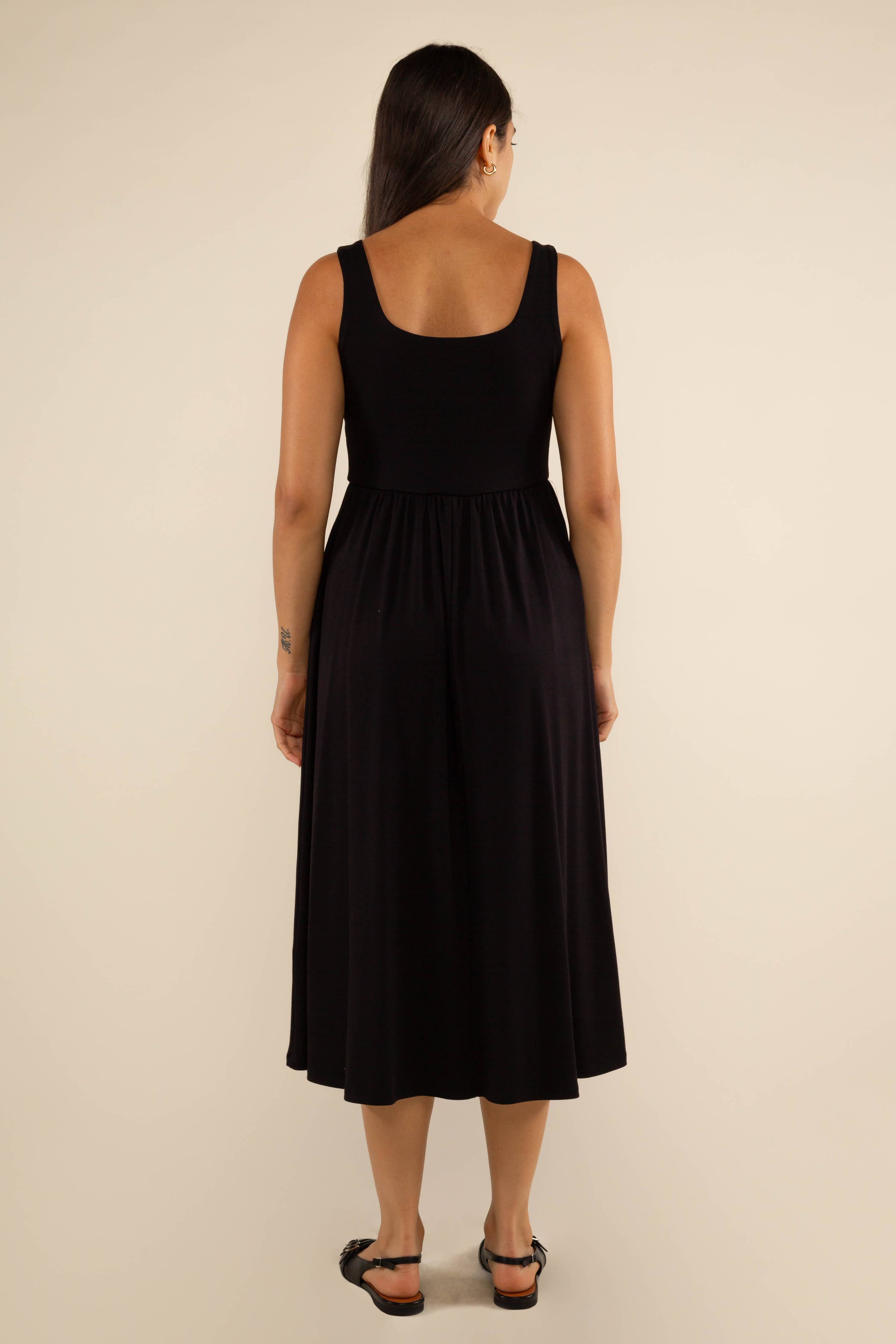 Woman facing away from the camera wearing black thick tank strapped top dress with full bodice and low drop skirt