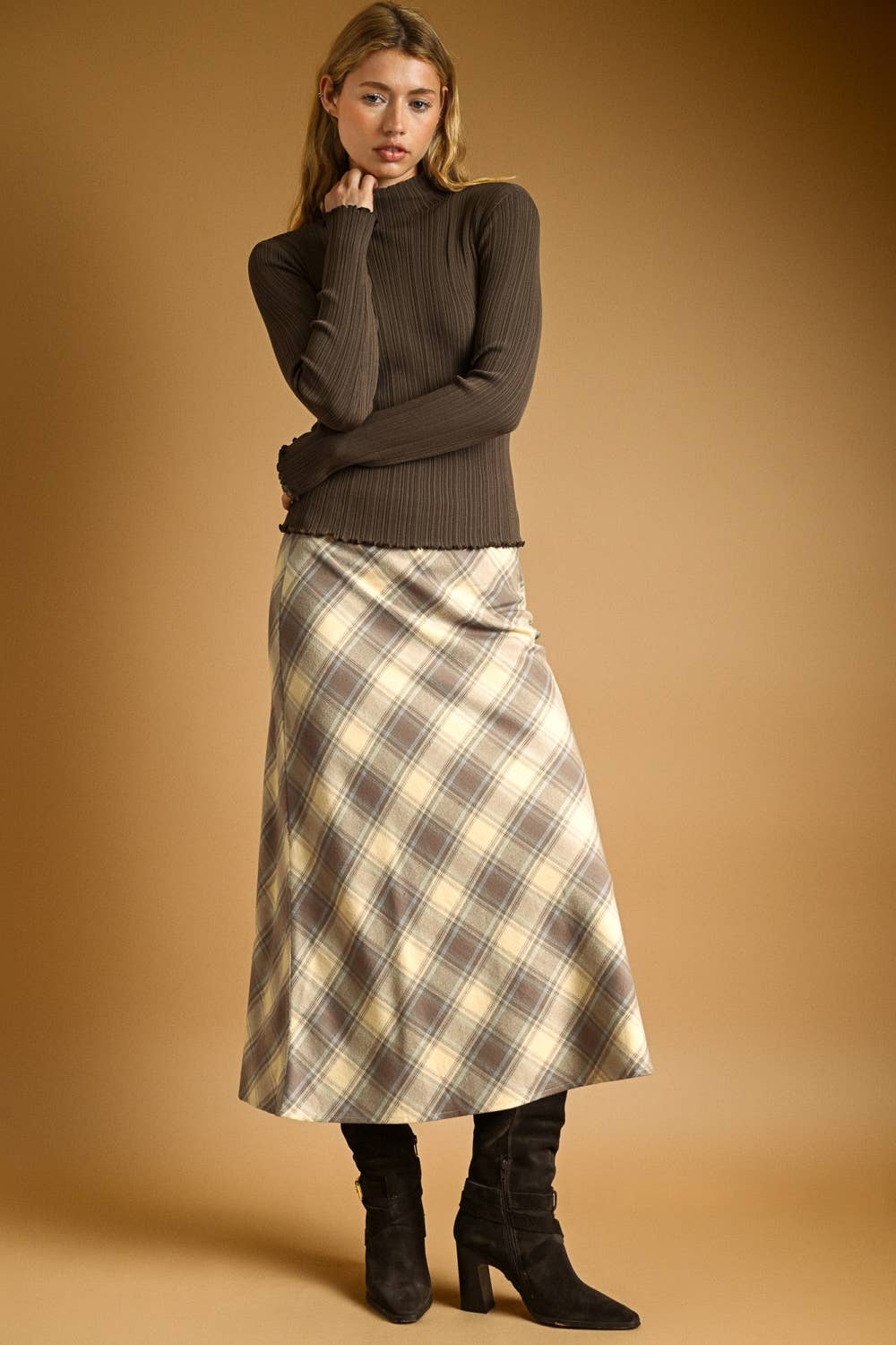 Woman wearing a brown ribbed sweater and plaid skirt against a beige background