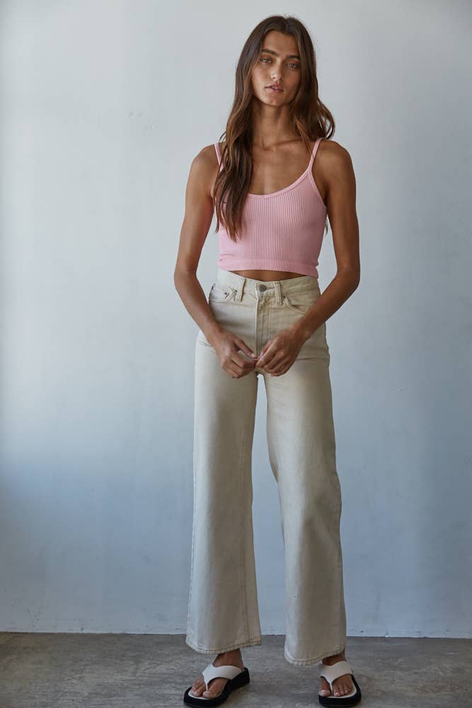 Woman wearing a pink tank top and beige pants against a plain background