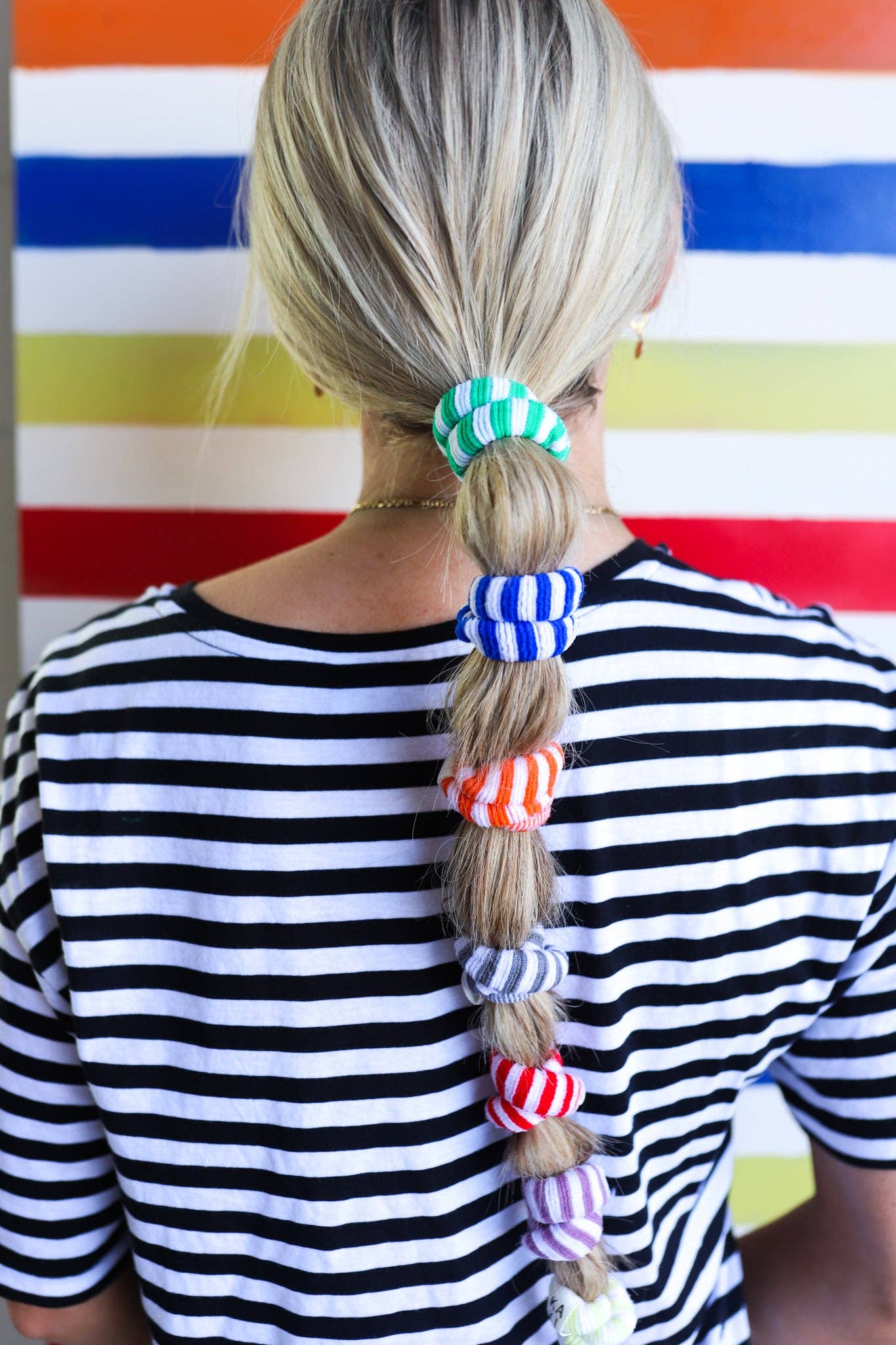 Person with colorful hair ties in a striped shirt against a striped background