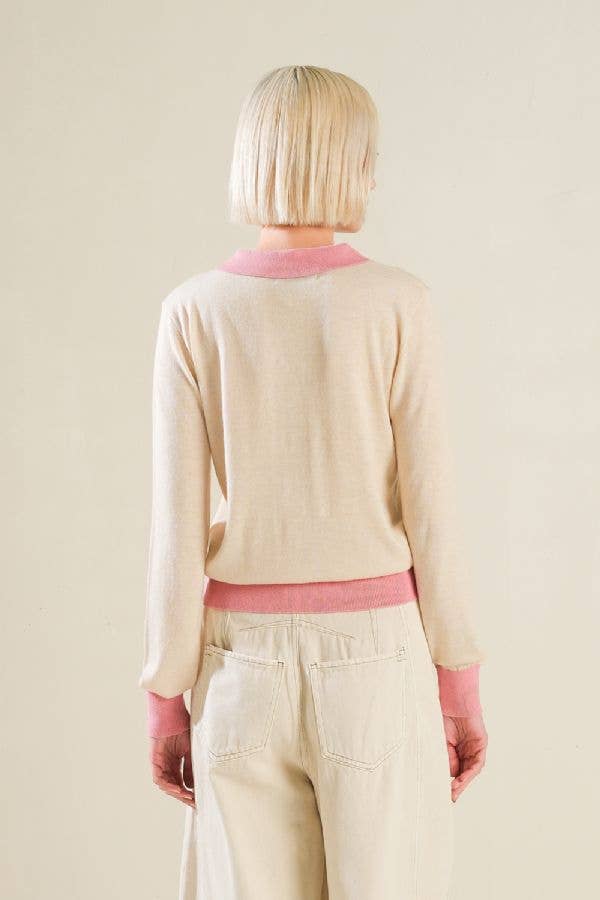 Person wearing a beige sweater with pink trim on a plain background