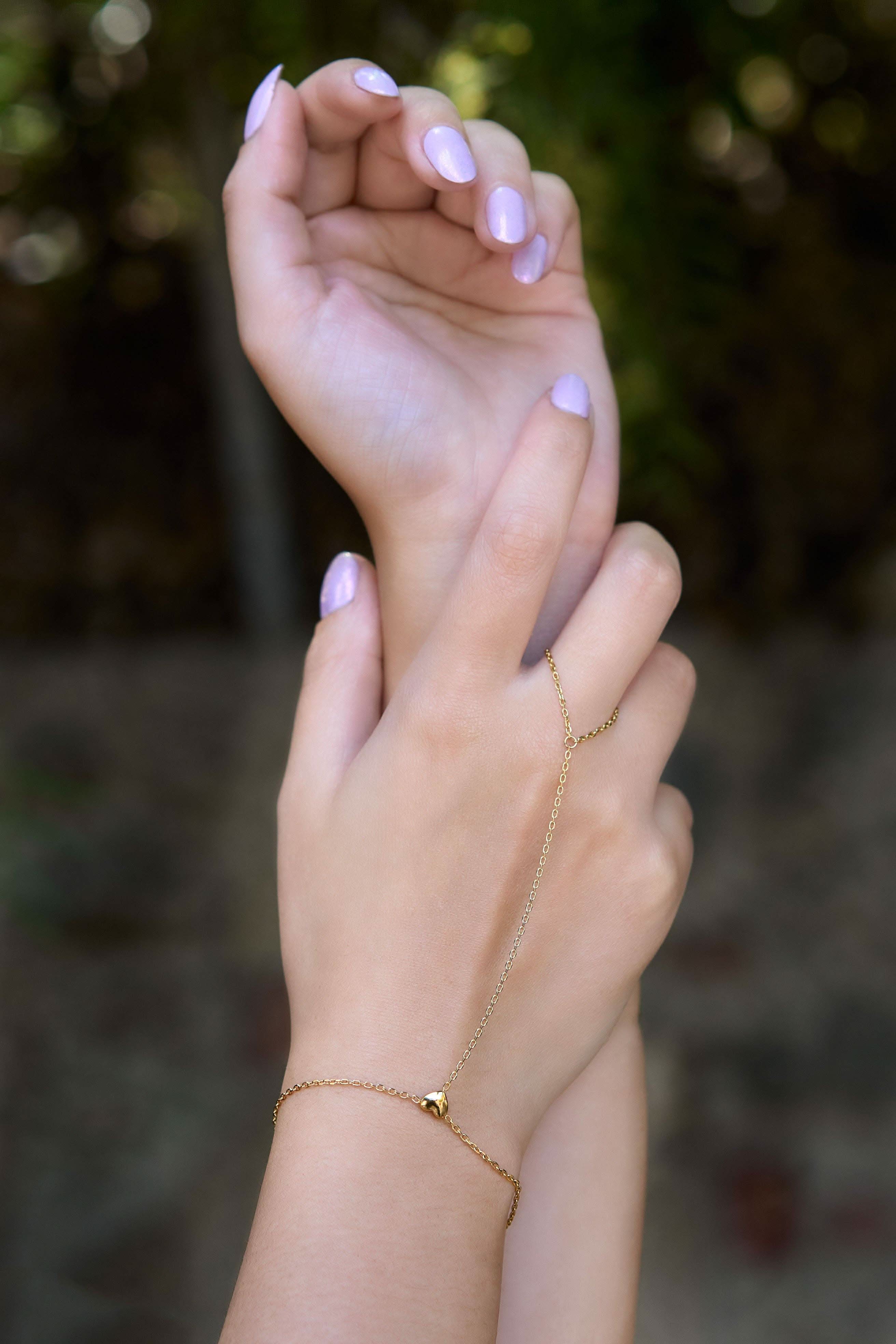 Delicate gold hand chain bracelet connected to a thin ring