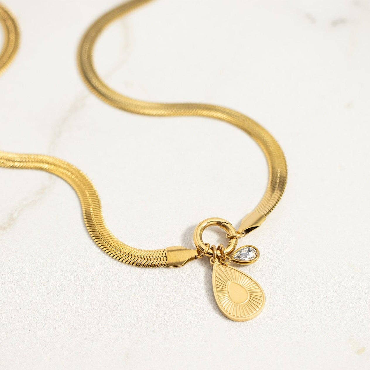 Gold bracelet with a teardrop charm on a light background