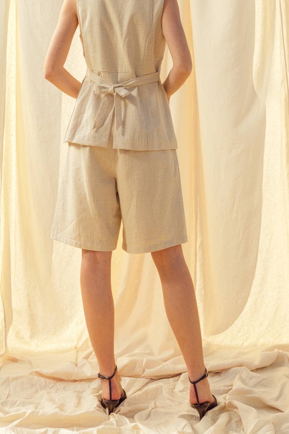 Person wearing a beige sleeveless top and shorts set on a soft, light-colored fabric background.