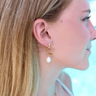 Woman wearing Waterproof gold huggie earrings with single Crystal gem in second piercing  