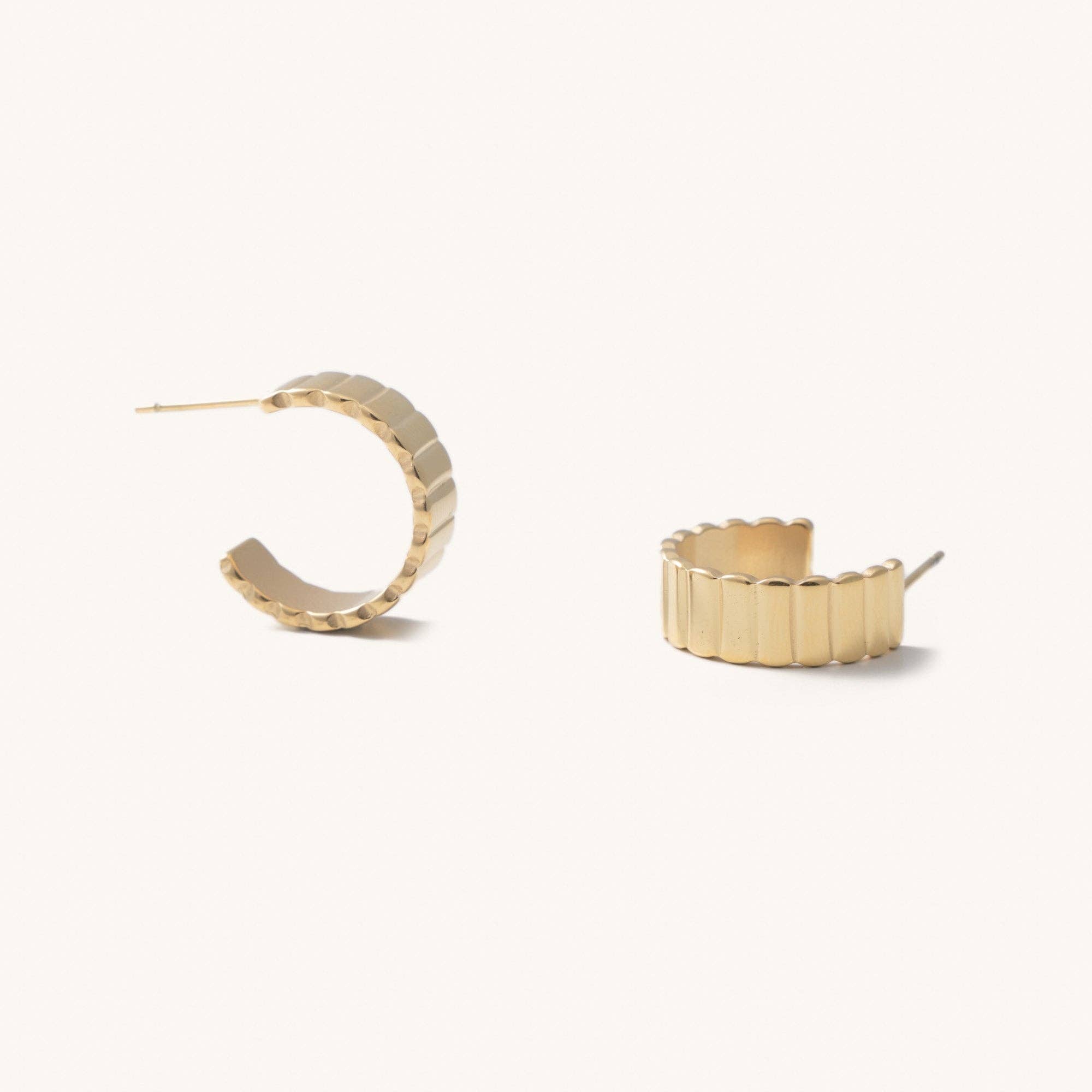 Gold ridged hoop earrings laying on a white background 