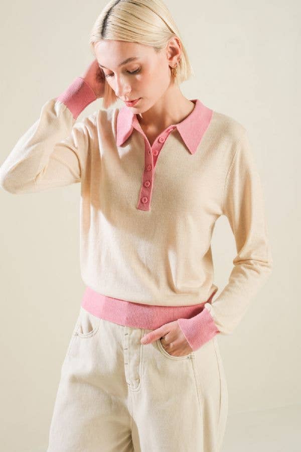 Woman wearing a beige sweater with pink collar and cuffs against a plain background