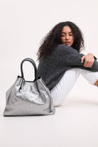 Model sitting down looking at silver metallic leather handbag with black strap