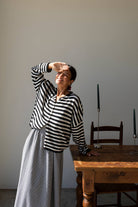 Woman leaning on a wooden table wearing long skirt and button down, black and white striped, cardigan 