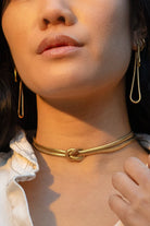 Woman wearing long abstract loop earrings and gold figure eight knot herringbone choker necklace 