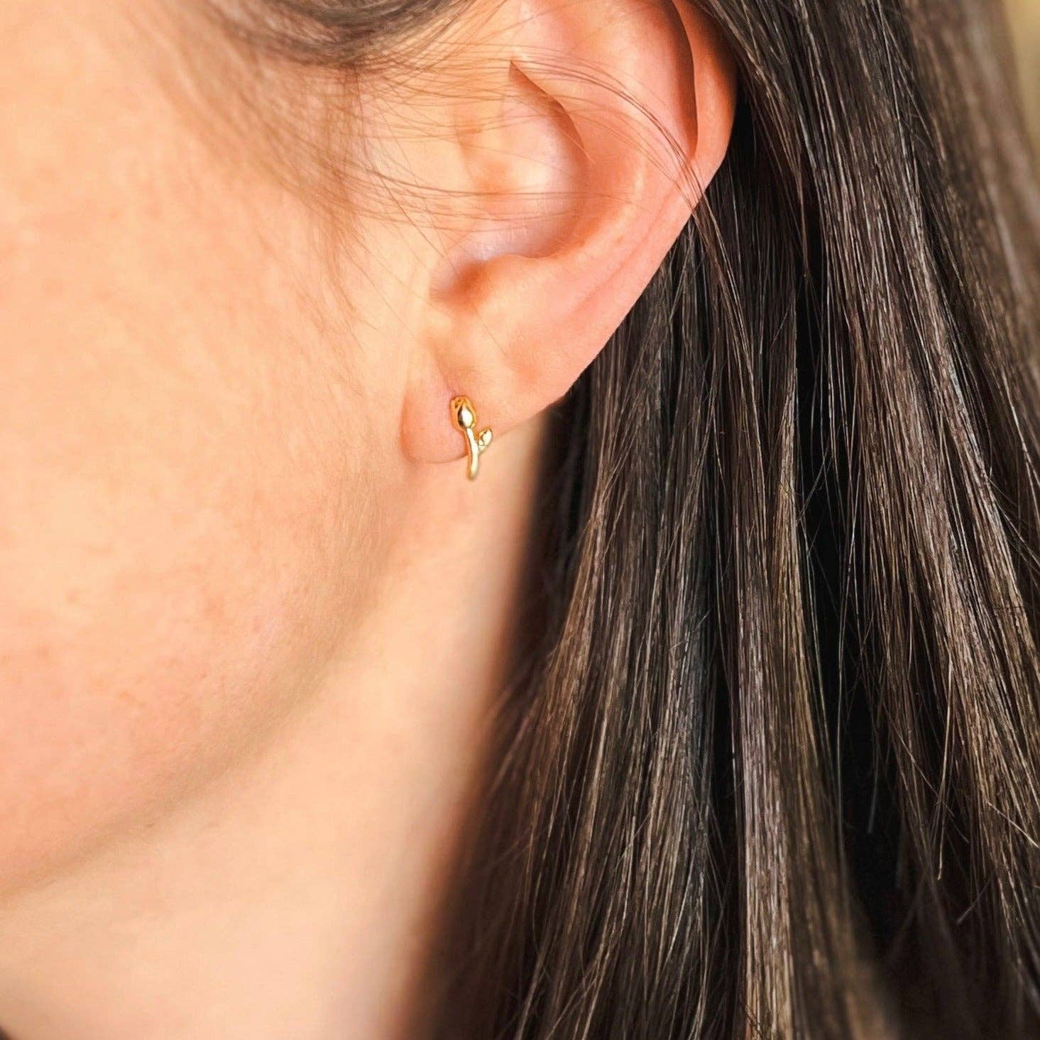 Close-up of an ear wearing a gold earring with hair partially obscuring the view.