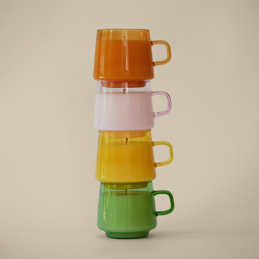 Four candles in orange, pink, yellow, and green opaque reusable mug sitting stacked on one another in the sun against a cream colored wall