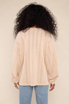Woman wearing lightweight, beige, cable knit detail, sweater/ sweatshirt and blue jeans 