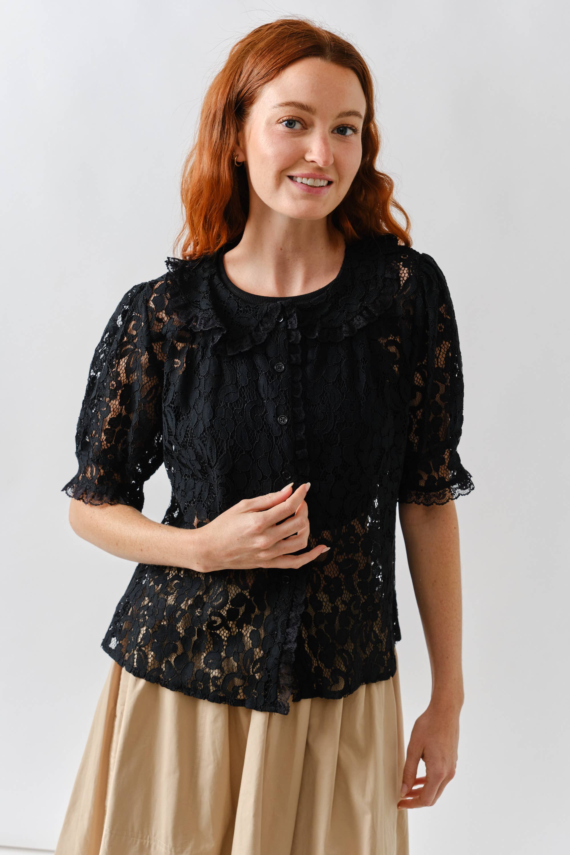 Woman wearing a black lace top and beige skirt against a white background