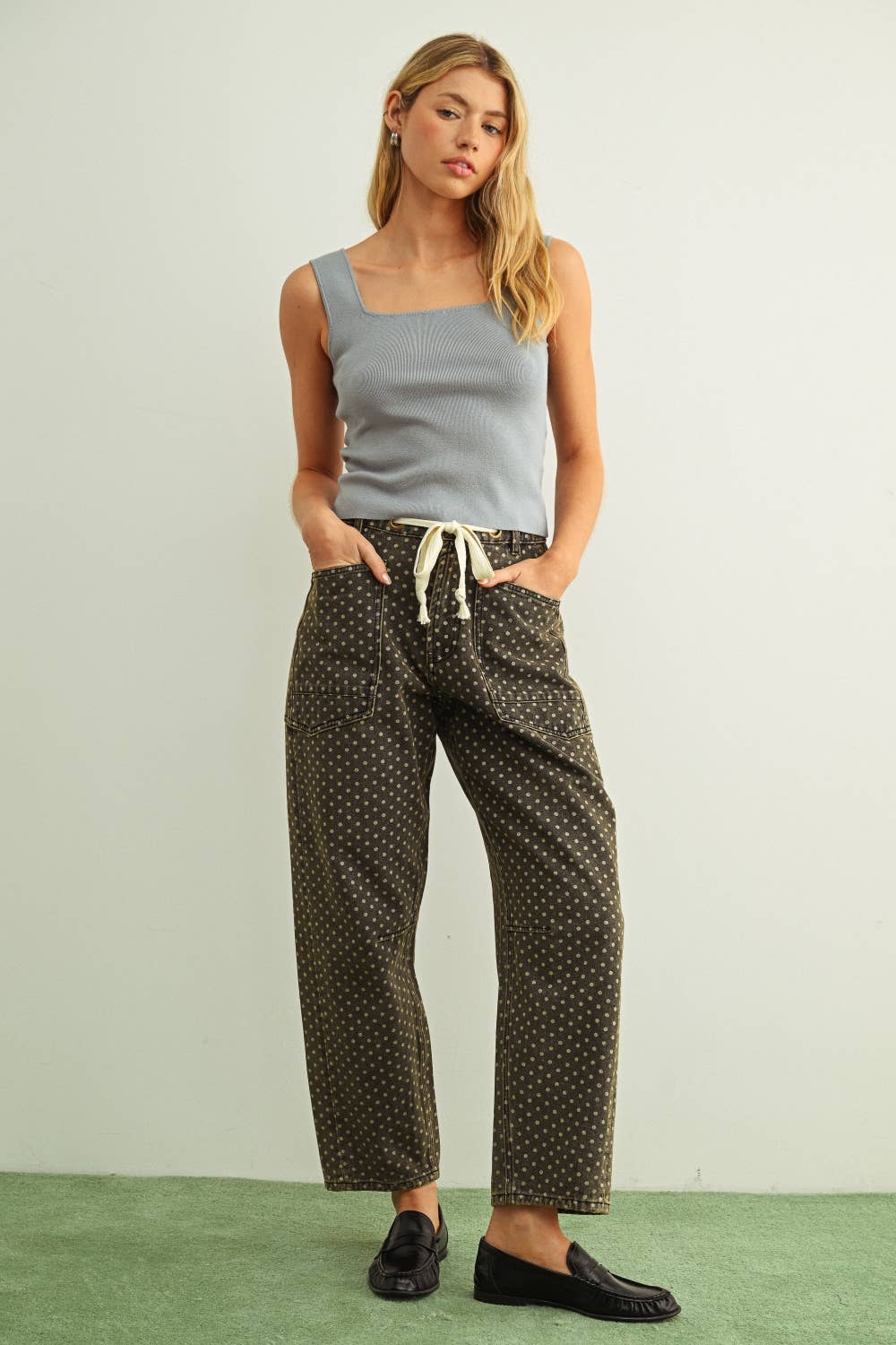Woman wearing a light blue tank top and patterned pants on a plain background