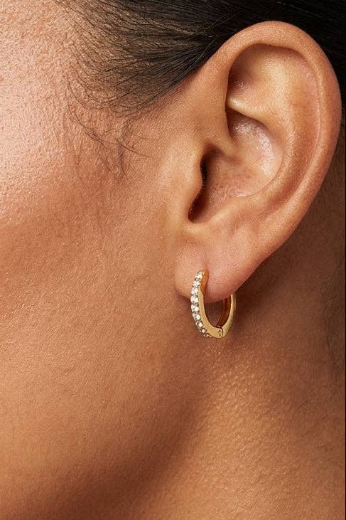 Close-up of an ear wearing a gold hoop earring with clear stones.