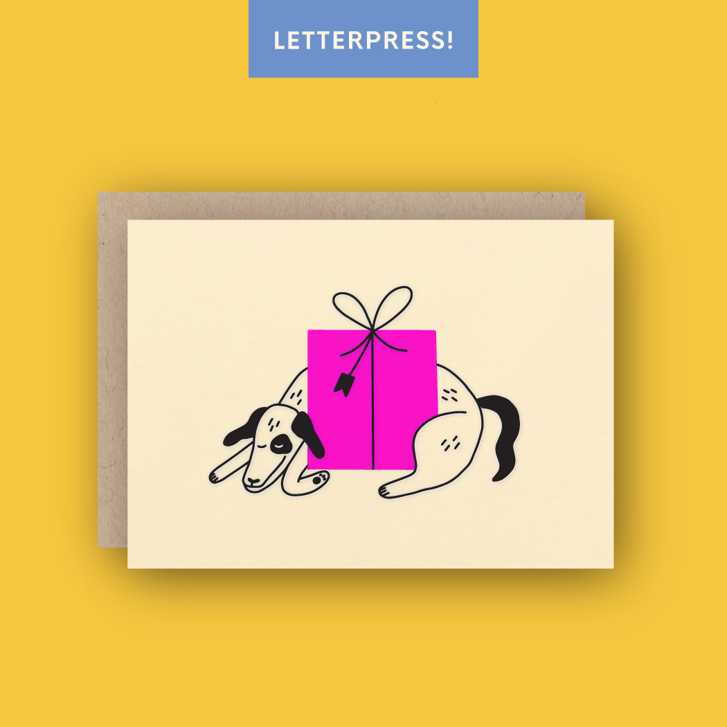 Letter press birthday greeting card picturing dog hugging pink present sitting against yellow background 