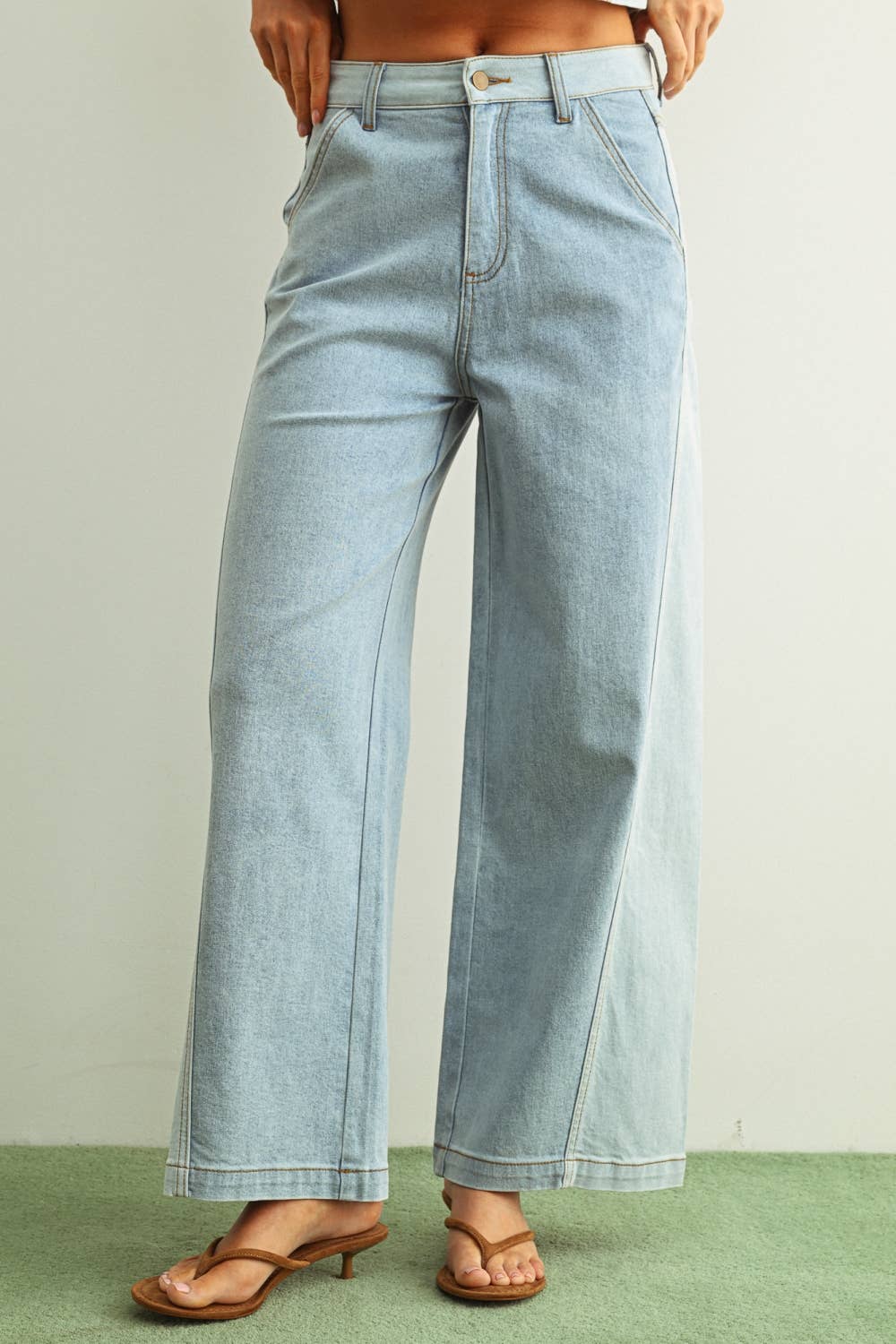 Woman wearing light denim jeans and light brown shoes standing behind a white background