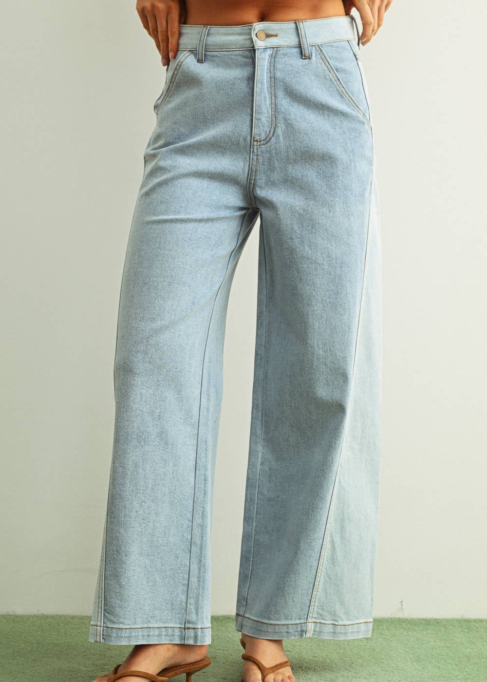 Woman wearing light denim jeans and light brown shoes standing behind a white background
