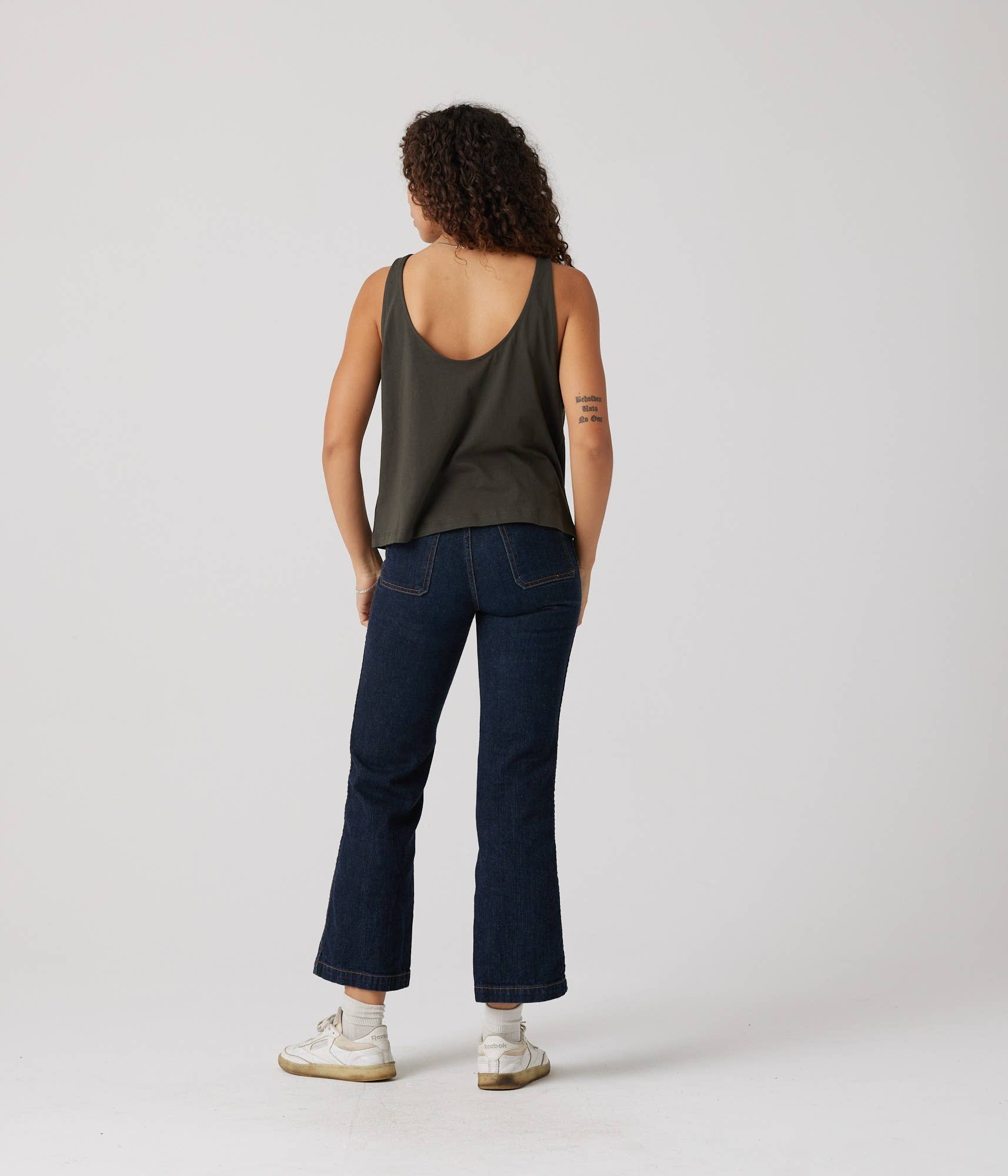 Person wearing a green tank top and dark blue jeans on a white background